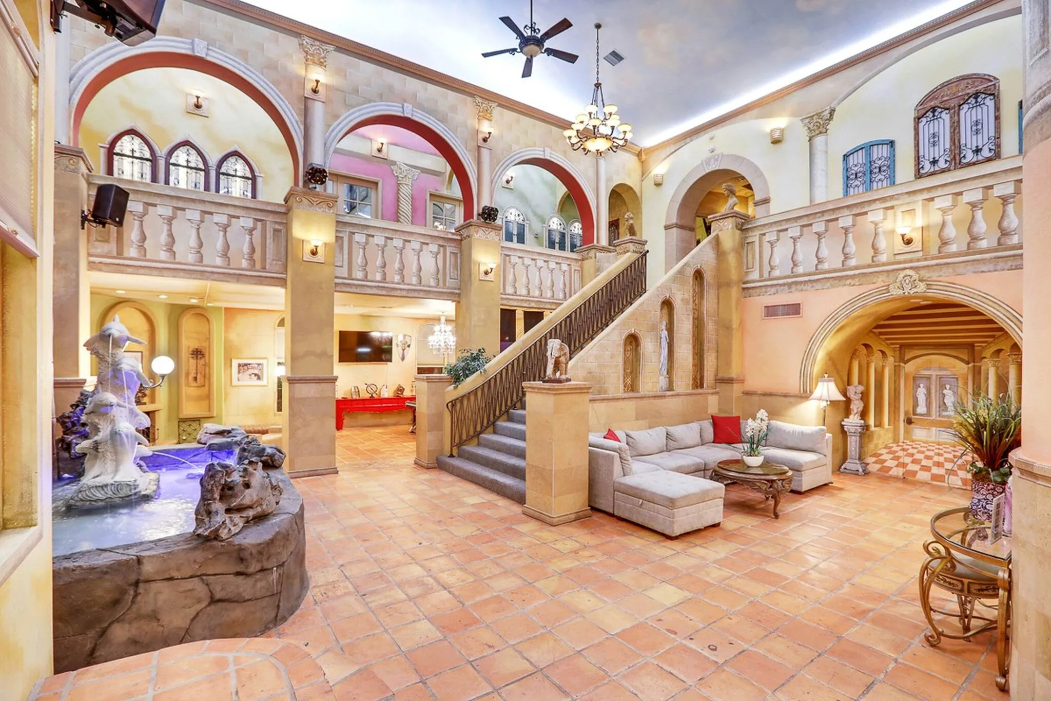 The grand entrance at D&D Mansion in Vegas features a Venetian-style stone staircase and railing, fountain, sofa seating, and arched corridors.