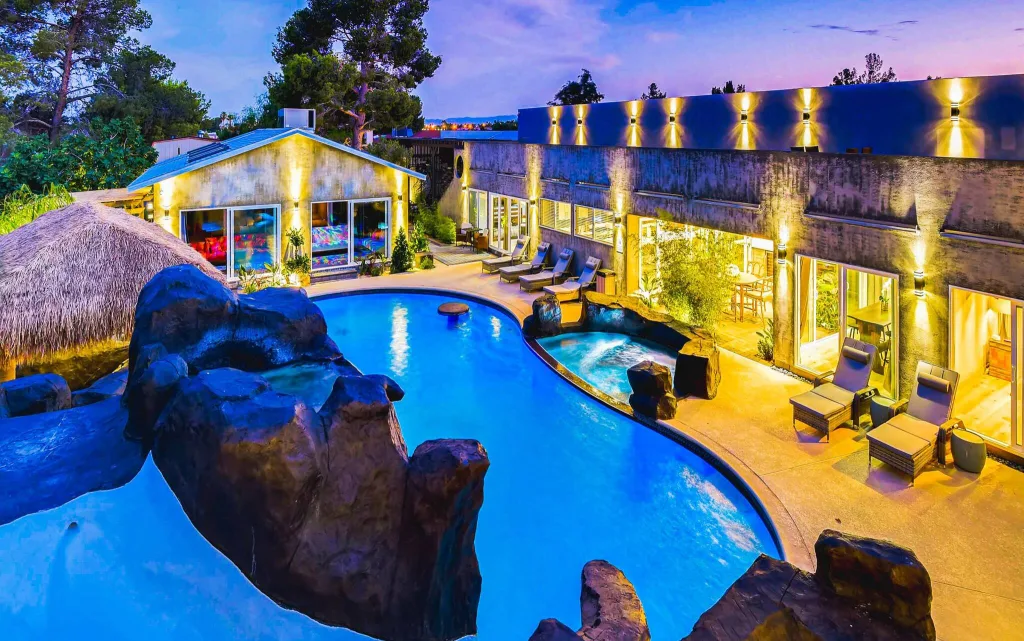 The pool with grotto at R&R Mansion seen from above, with the expansive villas in the background, and multiple loungers around the pool and hot tub.
