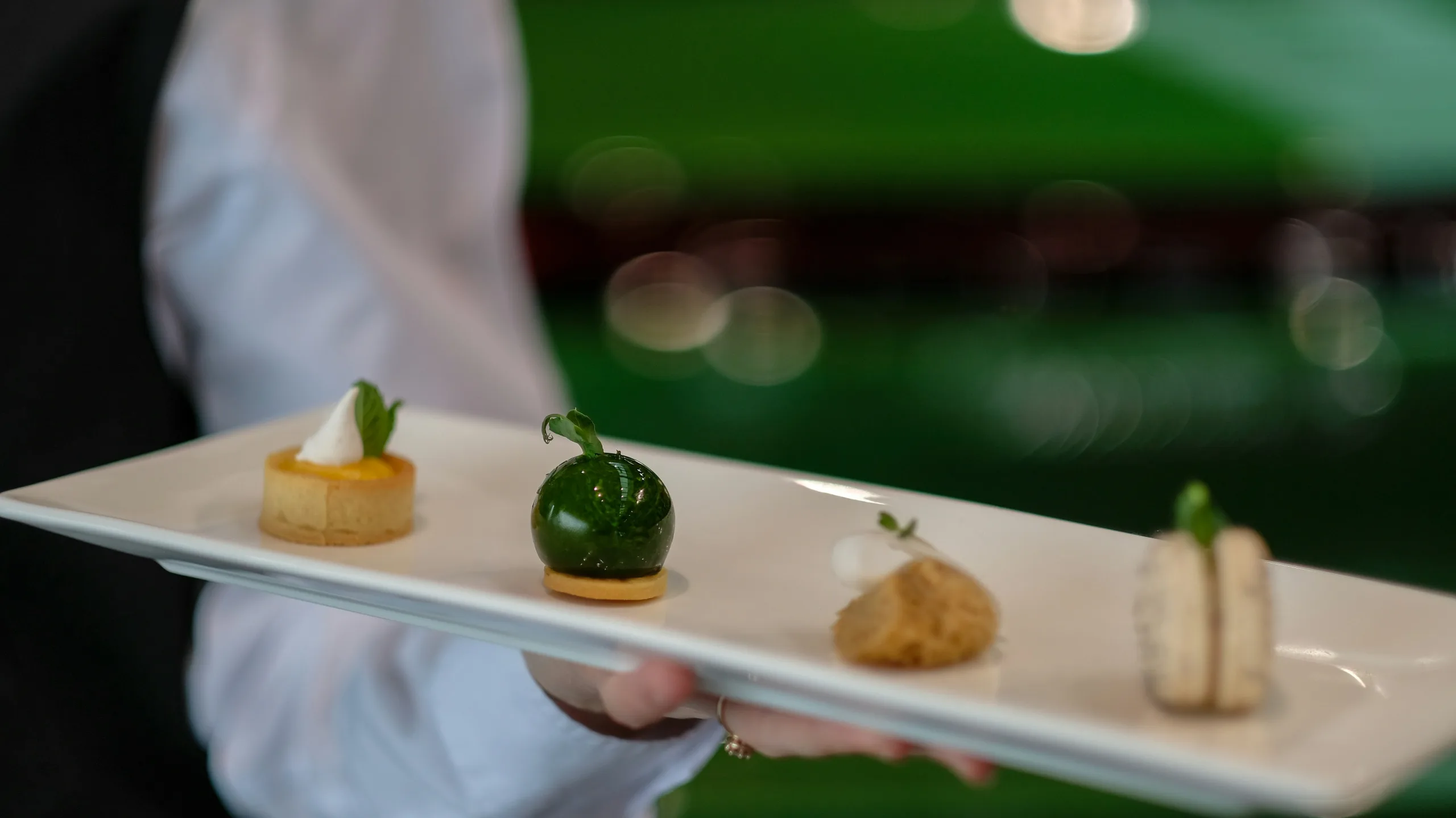 A caterer's hand holds a rectangular plate of elegant hors d'oeuvres