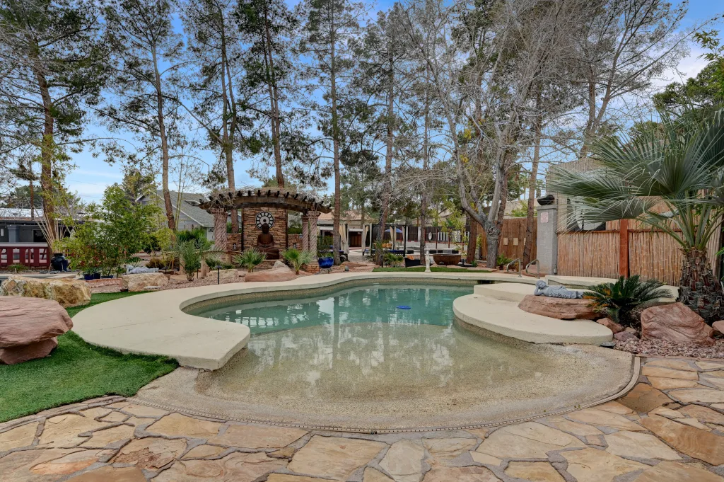 A pool and serene garden with tall trees with the Zen Oasis vacation house in the background