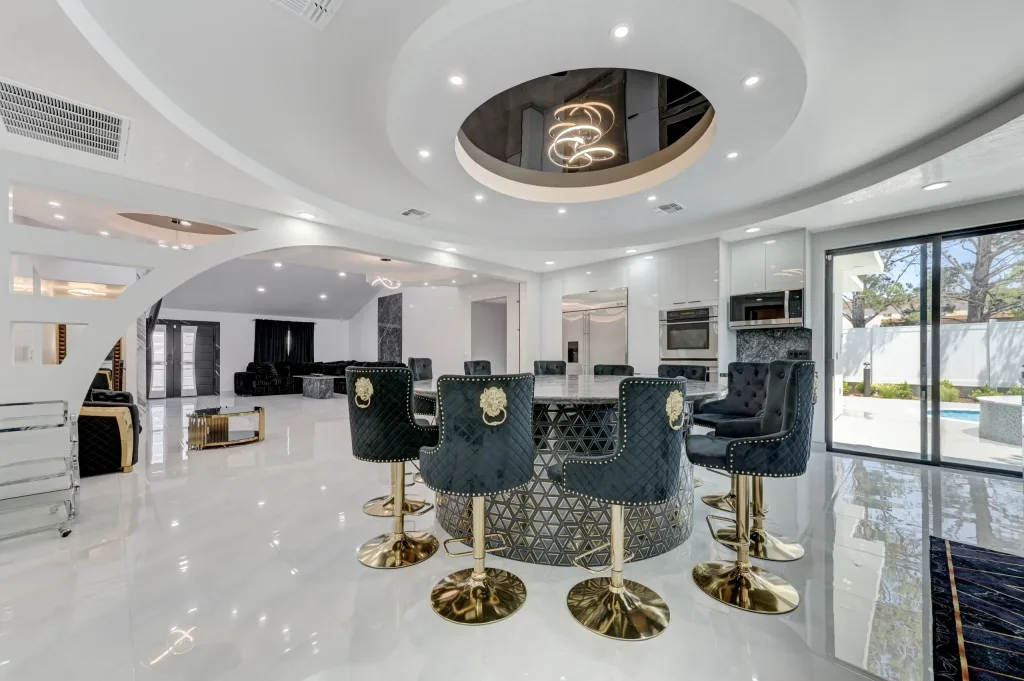 A modern bright interior of a dining space with white ceramic throuhgout and black leather bar seats with gold accents