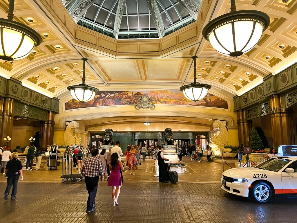 A grand outdoor entrance with domed ceiling and dome-shaped ceiling lamps greets visitors at the Bellagio, with guests arriving and cars stopping for pick ups.