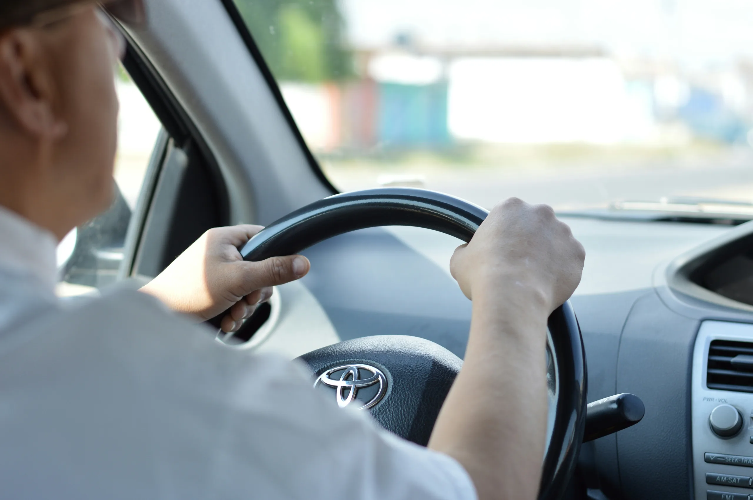 Taken from the backseat, a chauffeur wearing a white shirt is seen driving a car with both hands on the wheel
