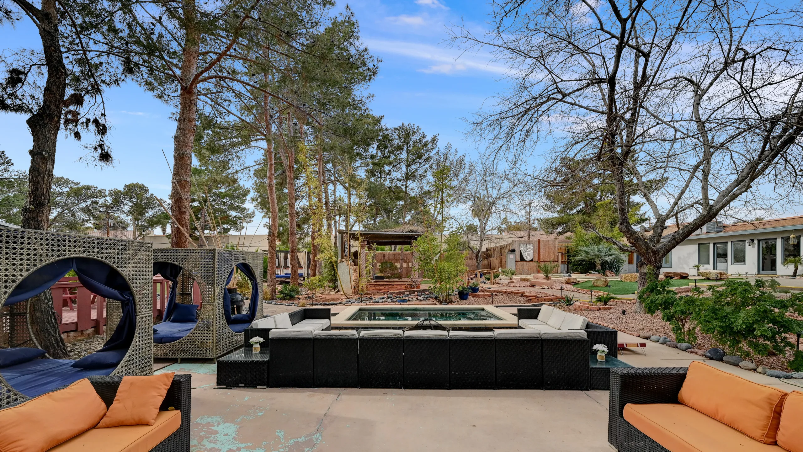 A raised plunge pool surrounded by outdoor sofas, pods for relaxing, and tall trees, in the backyard of Zen Paradise luxury villa in Vegas.